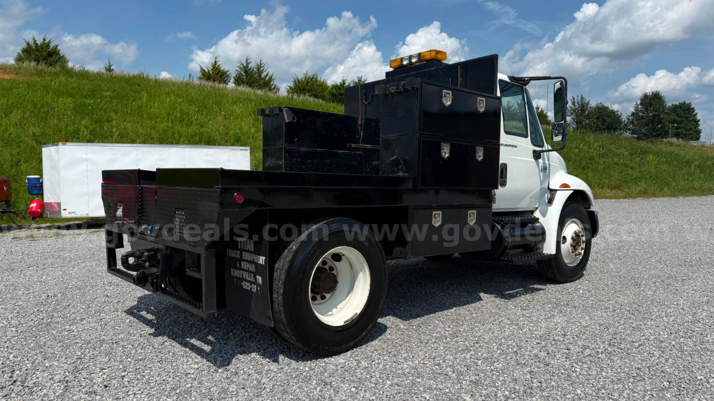 Flatbed tow truck side view showing heavy-duty toolbox compartments and black metal bed on a white International 4300 with white wheels.