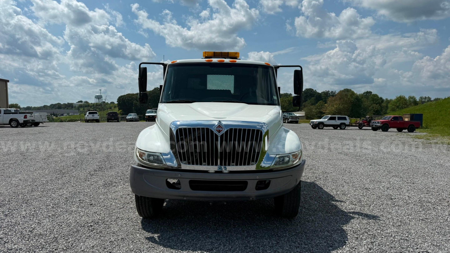 Truck front view of a white International 4300 flatbed with chrome grille and amber warning light on roof.