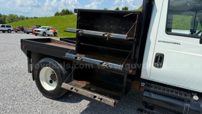 Flatbed truck showing toolbox compartments and open storage drawers on the passenger side of a 2007 International 4300 chassis, white cab, black metal utility bed.