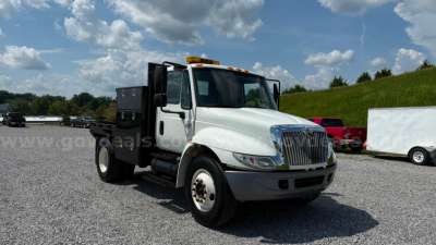 International 4300 flatbed truck in a used condition with white cab and black flatbed view from front-left angle.
