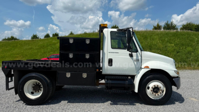 International 4300 flatbed truck side view showing tool boxes and cab, used 2007 model with white cab and black flatbed accessories.