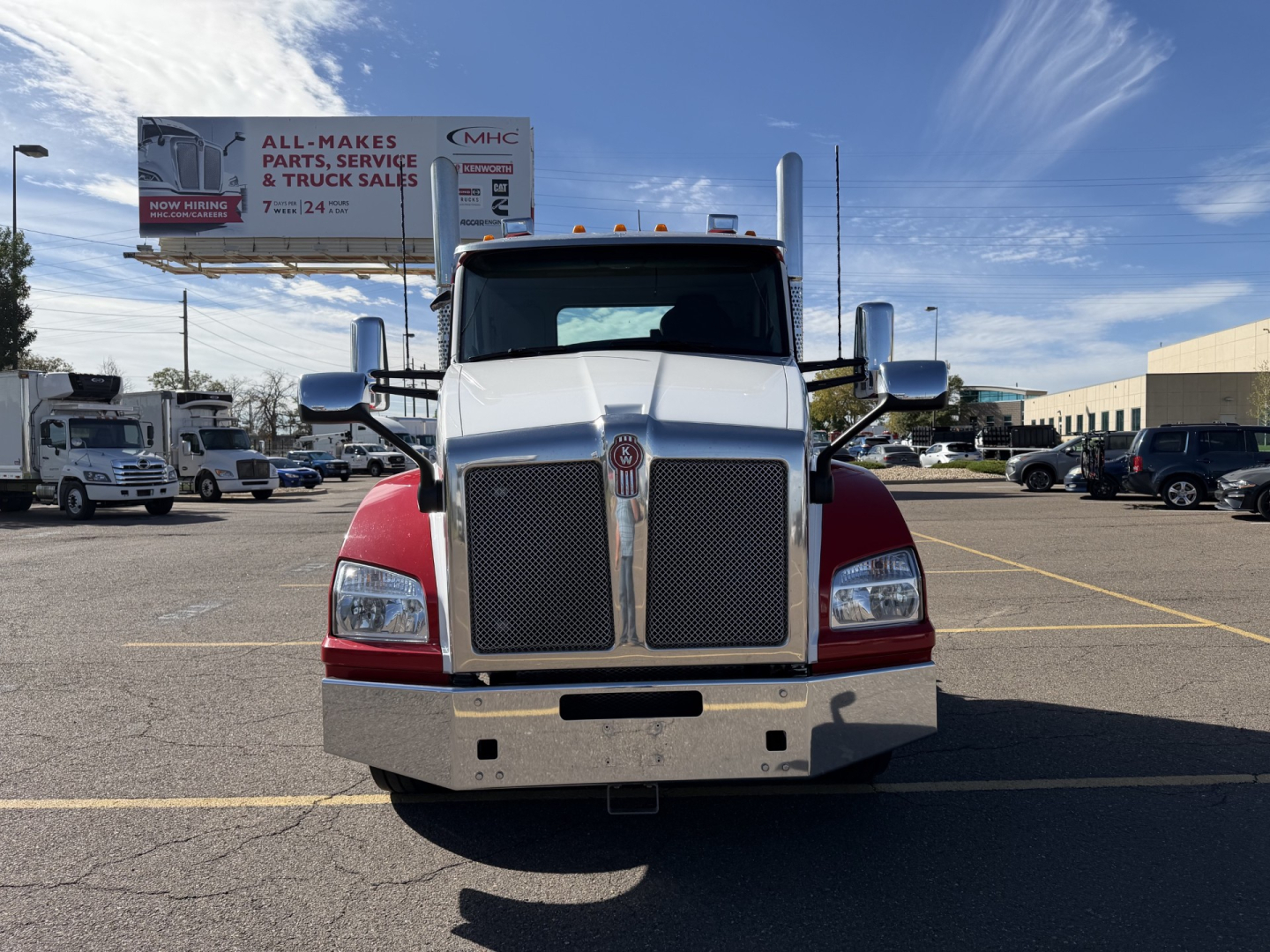 Front view of a white-and-red 2023 Kenworth T880 conventional daycab truck with large chrome grille, bumper, and mirrors in a dealership lot.