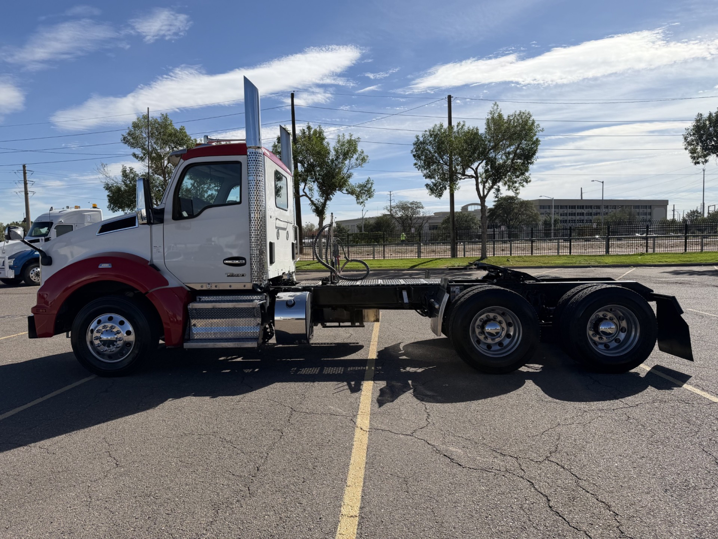 Kenworth T880 side view showing chassis with triple rear axles, cab with white and maroon color, fuel tanks, steps, and exhaust stack.