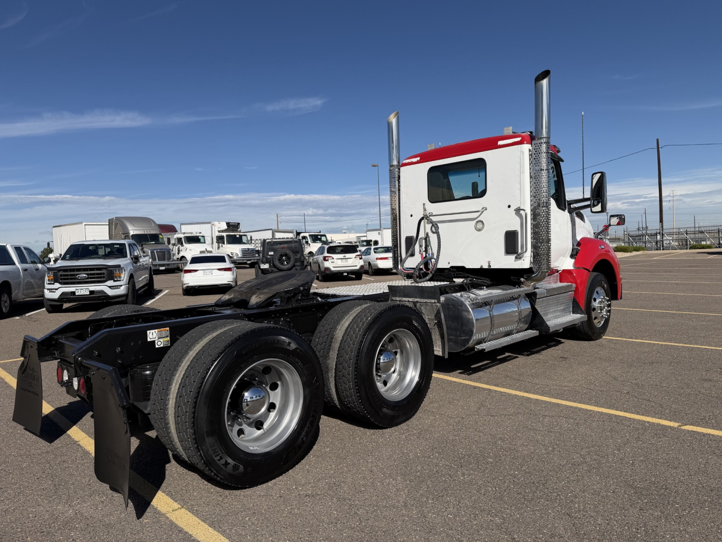 Kenworth T880 conventional daycab with red cab and white sleeper, rear view showing dual rear axles, fuel tanks, and fifth wheel in a parking lot.