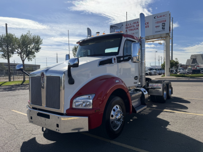 Kenworth T880 daycab truck in a parking lot, white cab with red fenders, chrome grille, stacked exhaust, and dual rear axles; front view with badge and mirrors visible.