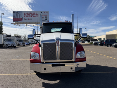 Front view of a white-and-red 2023 Kenworth T880 conventional daycab truck with large chrome grille, bumper, and mirrors in a dealership lot.