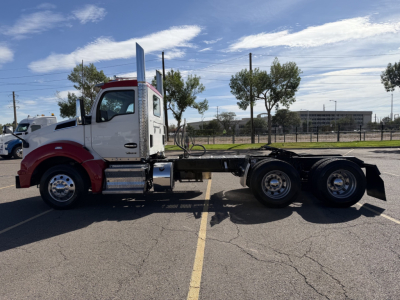 Kenworth T880 side view showing chassis with triple rear axles, cab with white and maroon color, fuel tanks, steps, and exhaust stack.
