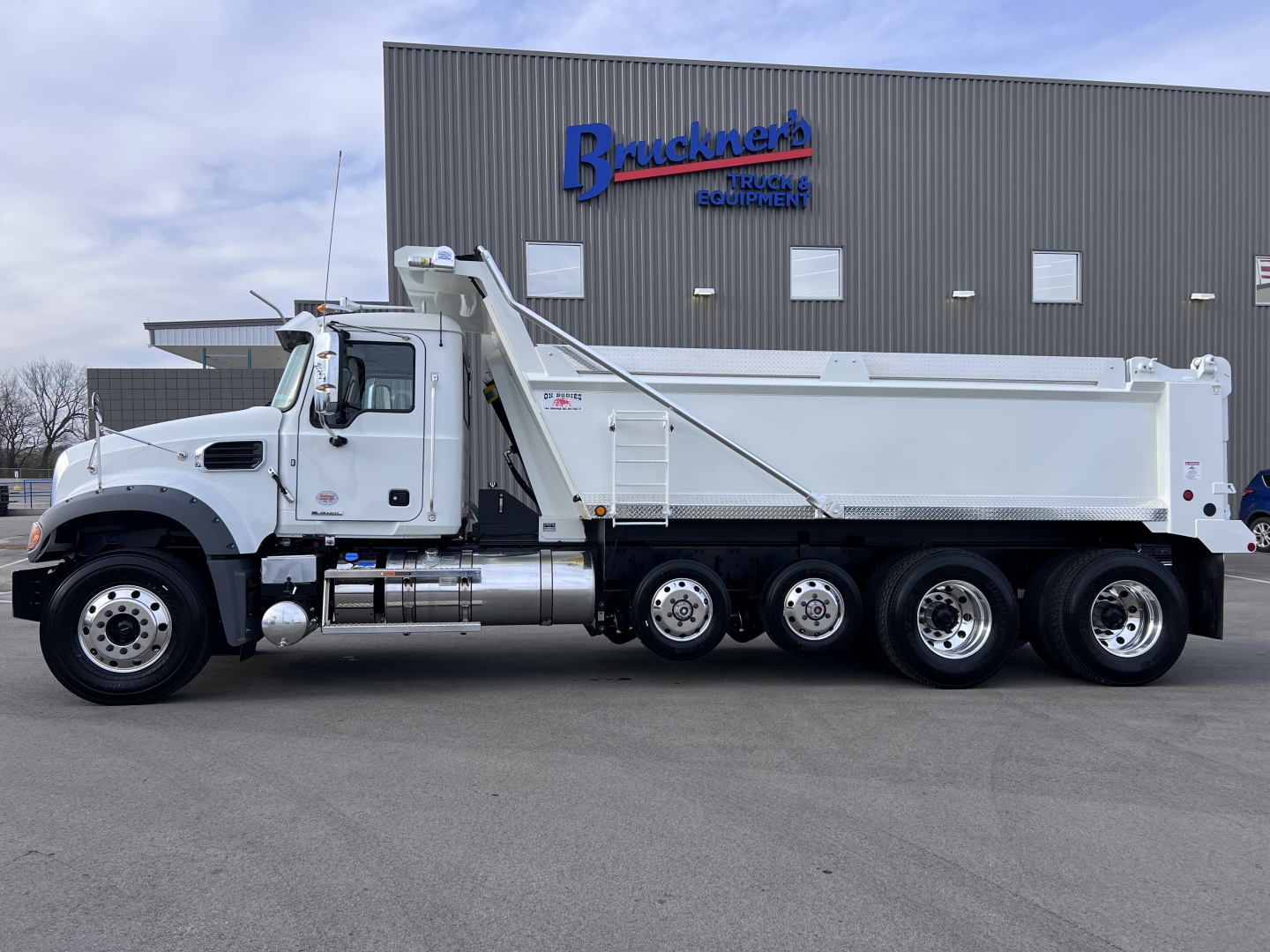 Mack GR64F dump truck in profile view showing side of dump body and rear wheels.