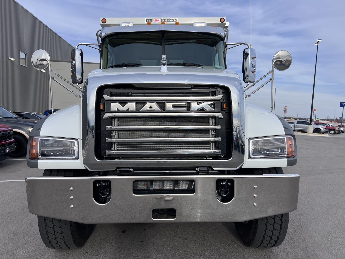 Mack GR64F front view showing large chrome grille with MACK emblem, dual rectangular headlights, heavy-duty bumper, and truck cab mirrors.