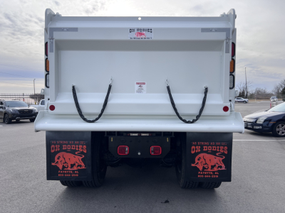 Rear view of a white Mack GR64F dump truck/ trailer showing the dump bed with two black straps, taillights, mud flaps with red graphics, and a license-free rear bumper area.