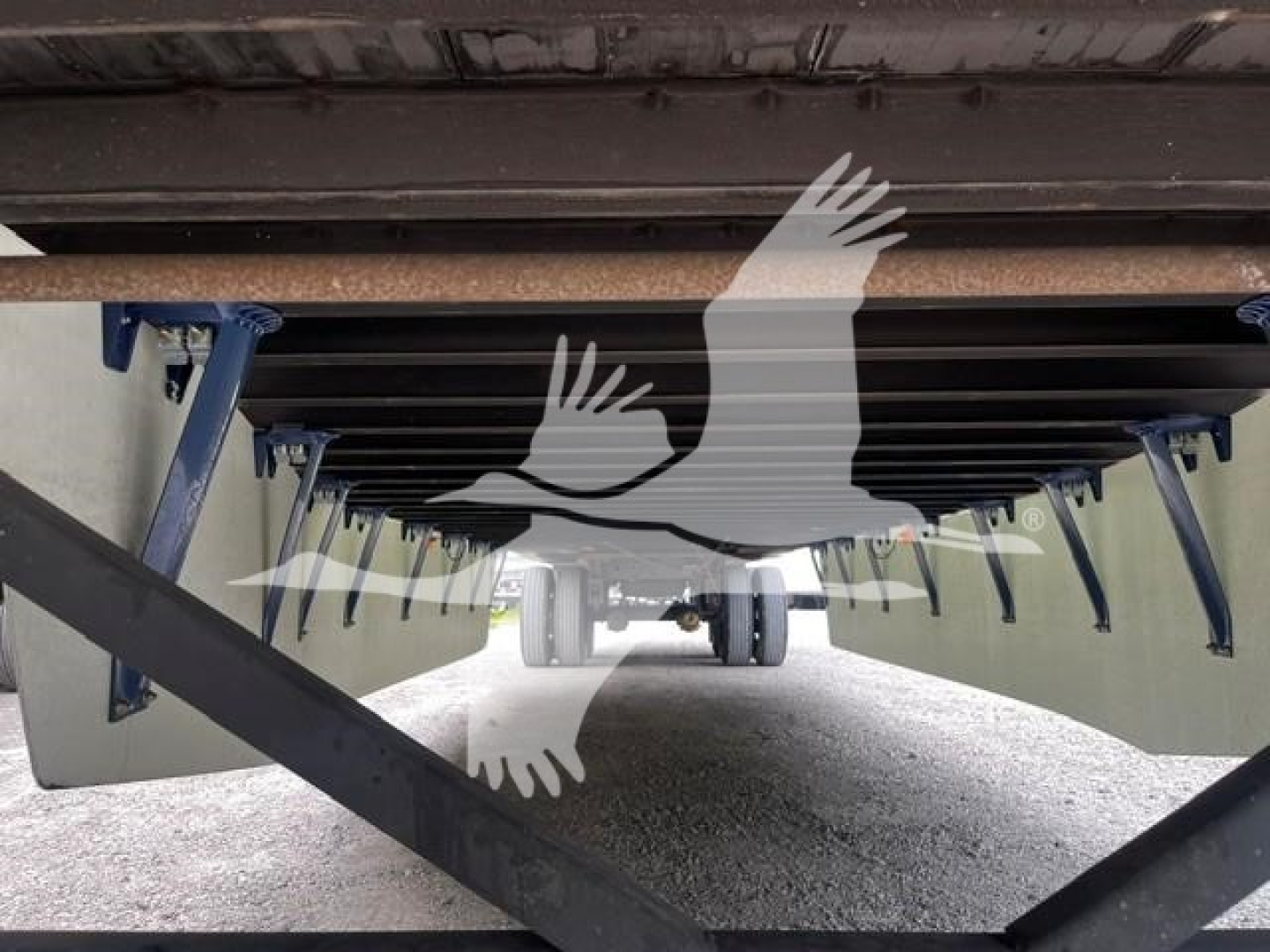 Trailer undercarriage view showing support legs and cross members of a dry van trailer, undercarriage underside with blue supports and gravel ground.
