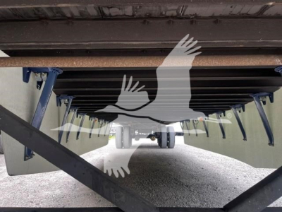 Trailer undercarriage view showing support legs and cross members of a dry van trailer, undercarriage underside with blue supports and gravel ground.