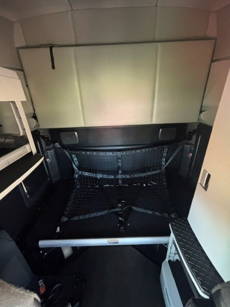 Truck cab interior cargo area showing storage compartments, bed area, and netting behind driver seat in a Kenworth T680 (cab/sleeper)
