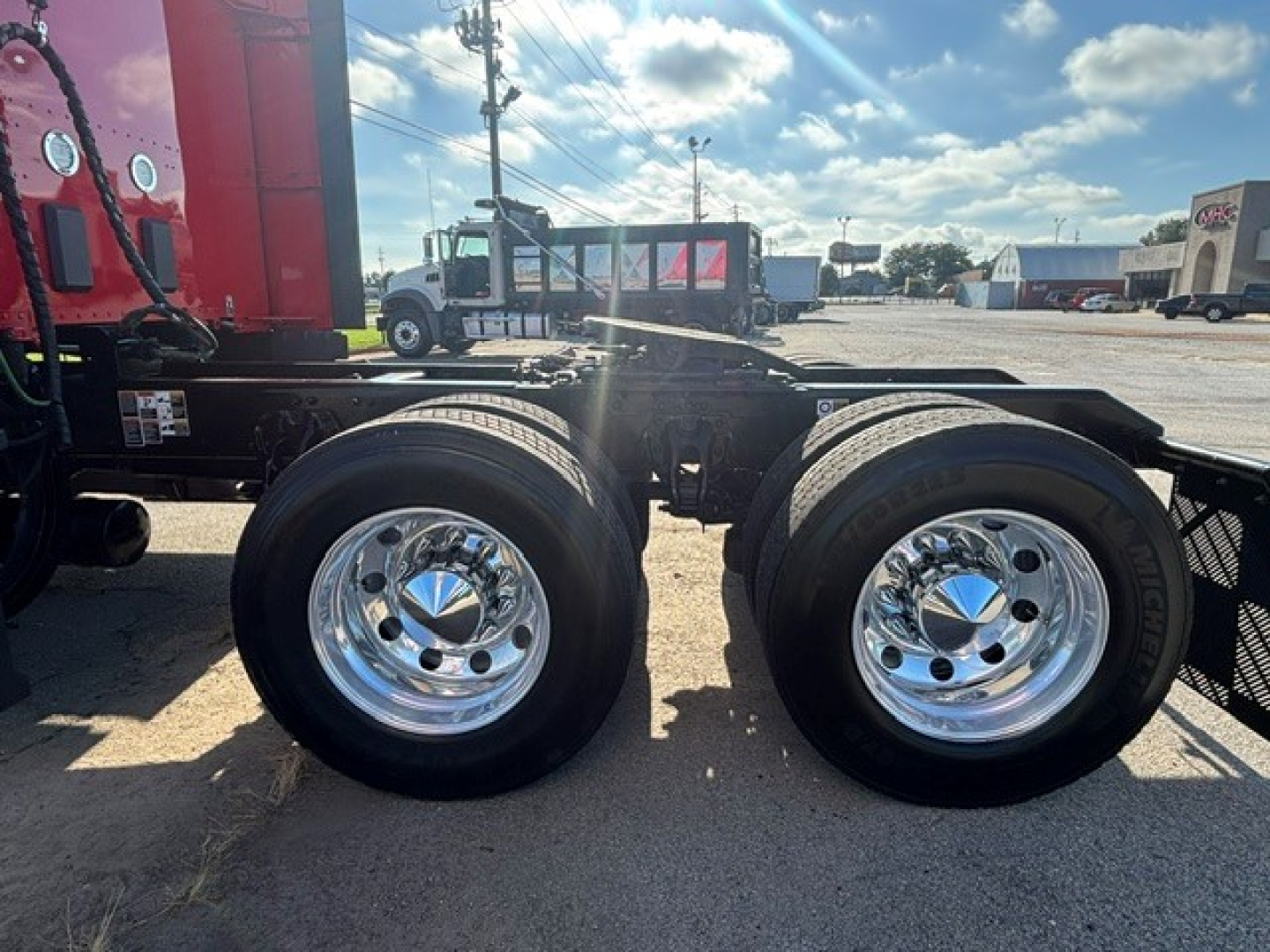 Kenworth T680 chassis dual rear wheels showing polished chrome rims and tires, with semi-truck cab and other equipment in background.