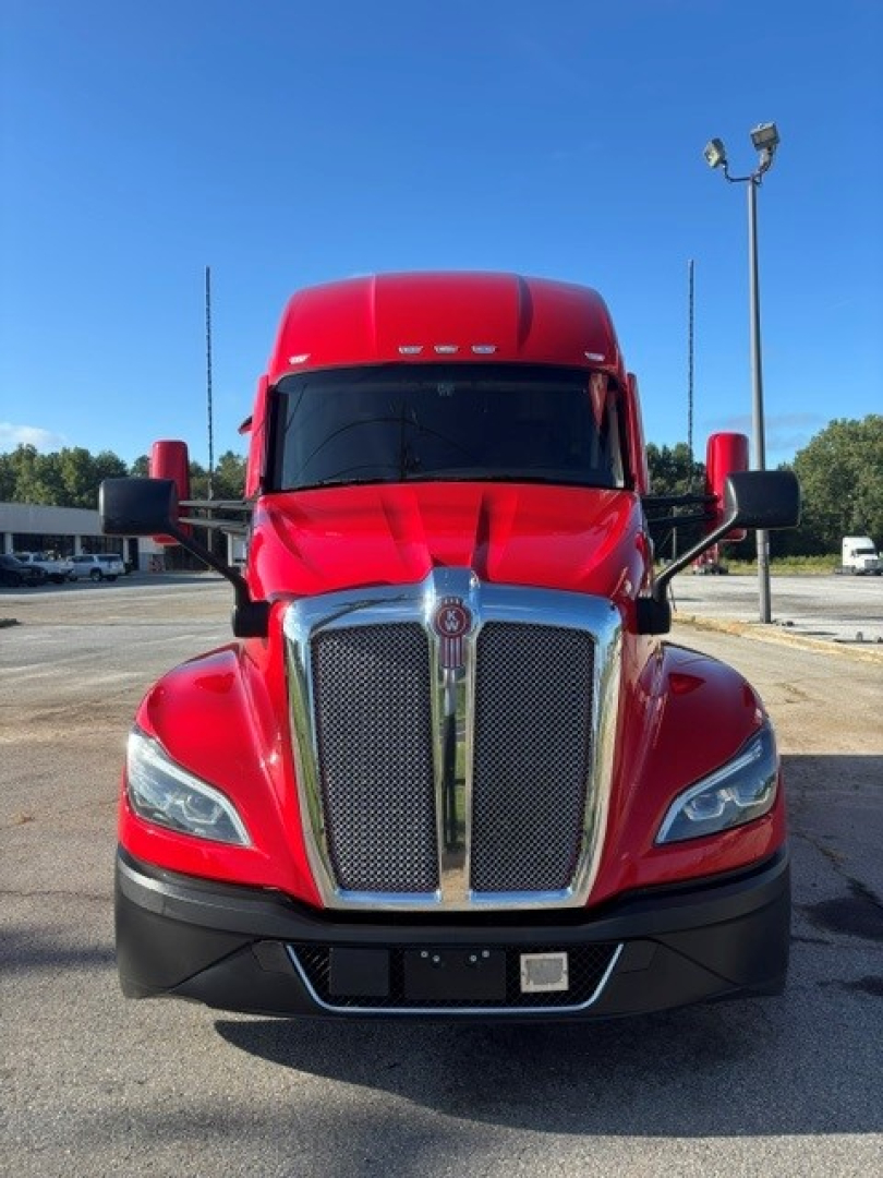 Kenworth T680 front view showing large chrome grille and red cab with black bumper, side mirrors, and headlights.