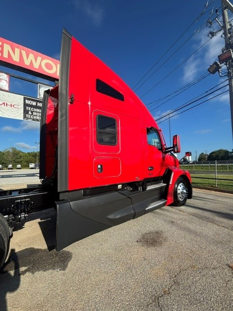 Kenworth T680 side cab view showing red sleeper and black chassis, with rear of truck and open trailer connection.