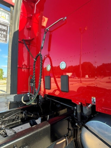 Kenworth T680 side view showing red tractor cab with external wiring and connection panels near the front, undercarriage and frame visible.