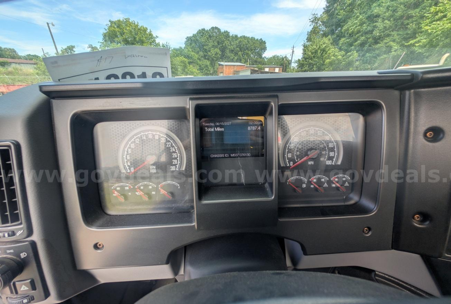 Mack MD truck dashboard gauge cluster with central touchscreen display showing text, two round gauges on either side, and warning indicators.