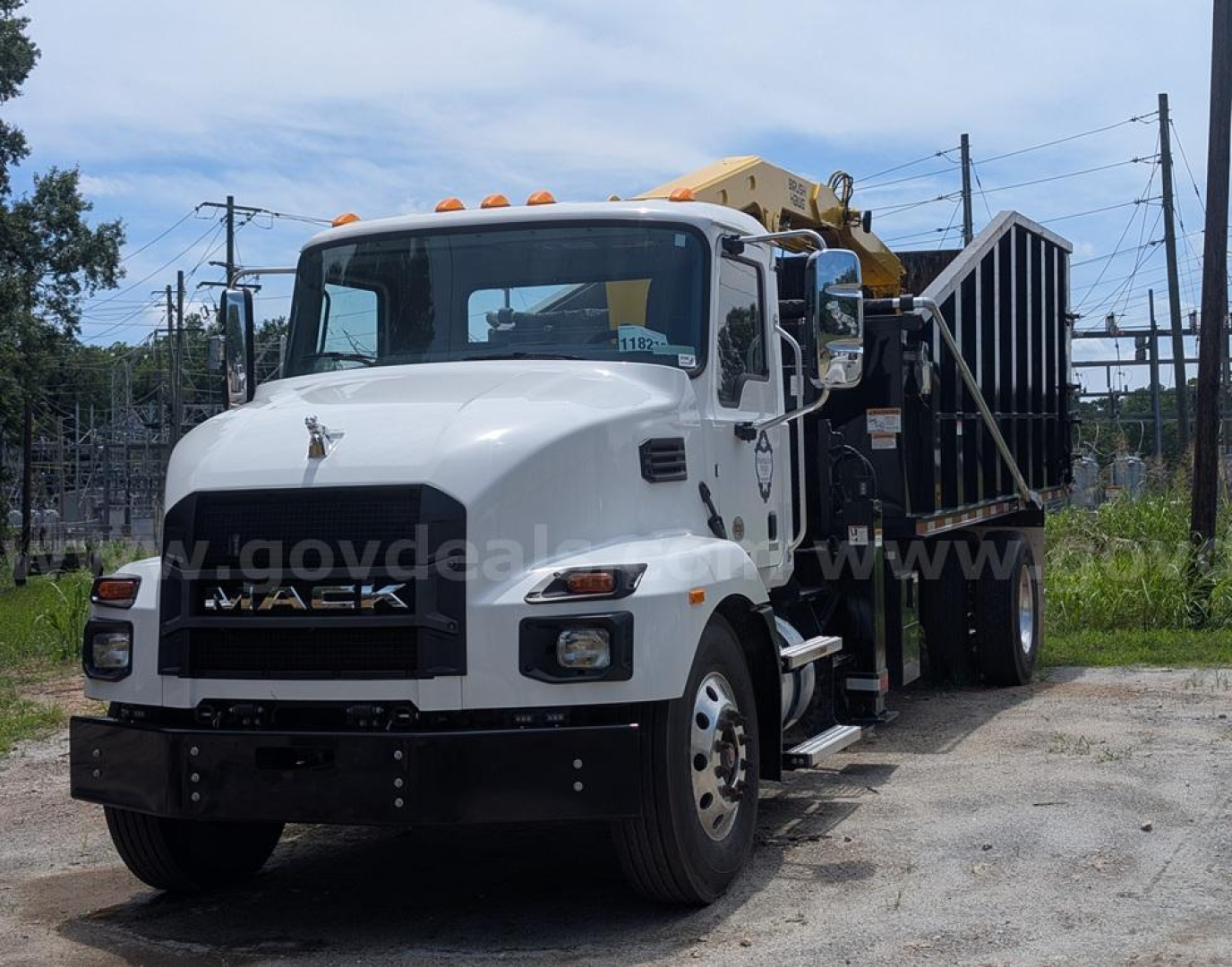 Mack MD truck with a grapple, white cab, dumping bed, and crane on the rear showing front view.