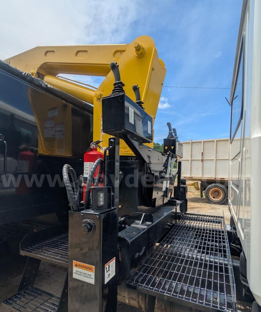 Mack MD grapple truck setup with control box and safety decals, platform grating visible, hydraulic components and yellow grapple arm in background.