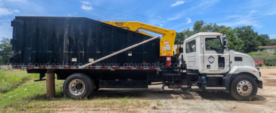 Truck side view showing a white Mack MD grapple truck with a yellow hydraulic crane mounted over a black dump bed.