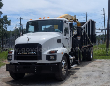 Mack MD truck with a grapple, white cab, dumping bed, and crane on the rear showing front view.