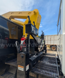 Mack MD grapple truck setup with control box and safety decals, platform grating visible, hydraulic components and yellow grapple arm in background.