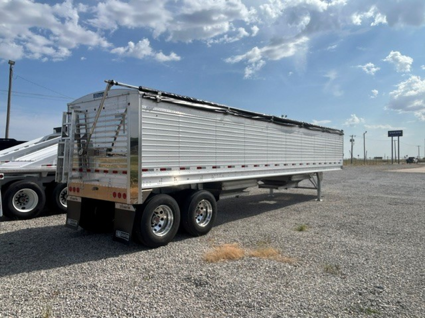 New Stoughton 40' aluminum grain hopper trailer with 68" corrugated sidewalls, triple-axle set, side ladders, and rear ramp in a gravel lot.
