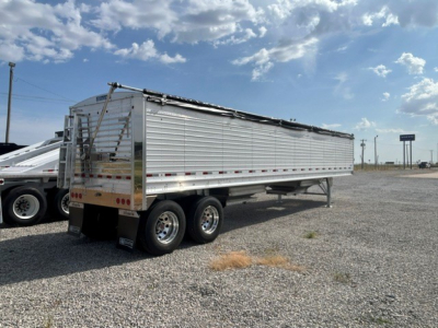 New Stoughton 40' aluminum grain hopper trailer with 68" corrugated sidewalls, triple-axle set, side ladders, and rear ramp in a gravel lot.