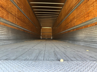 Hyundai 2017 dry van trailer interior view showing wooden side walls, metal rails, and ribbed floor with light at the far end.