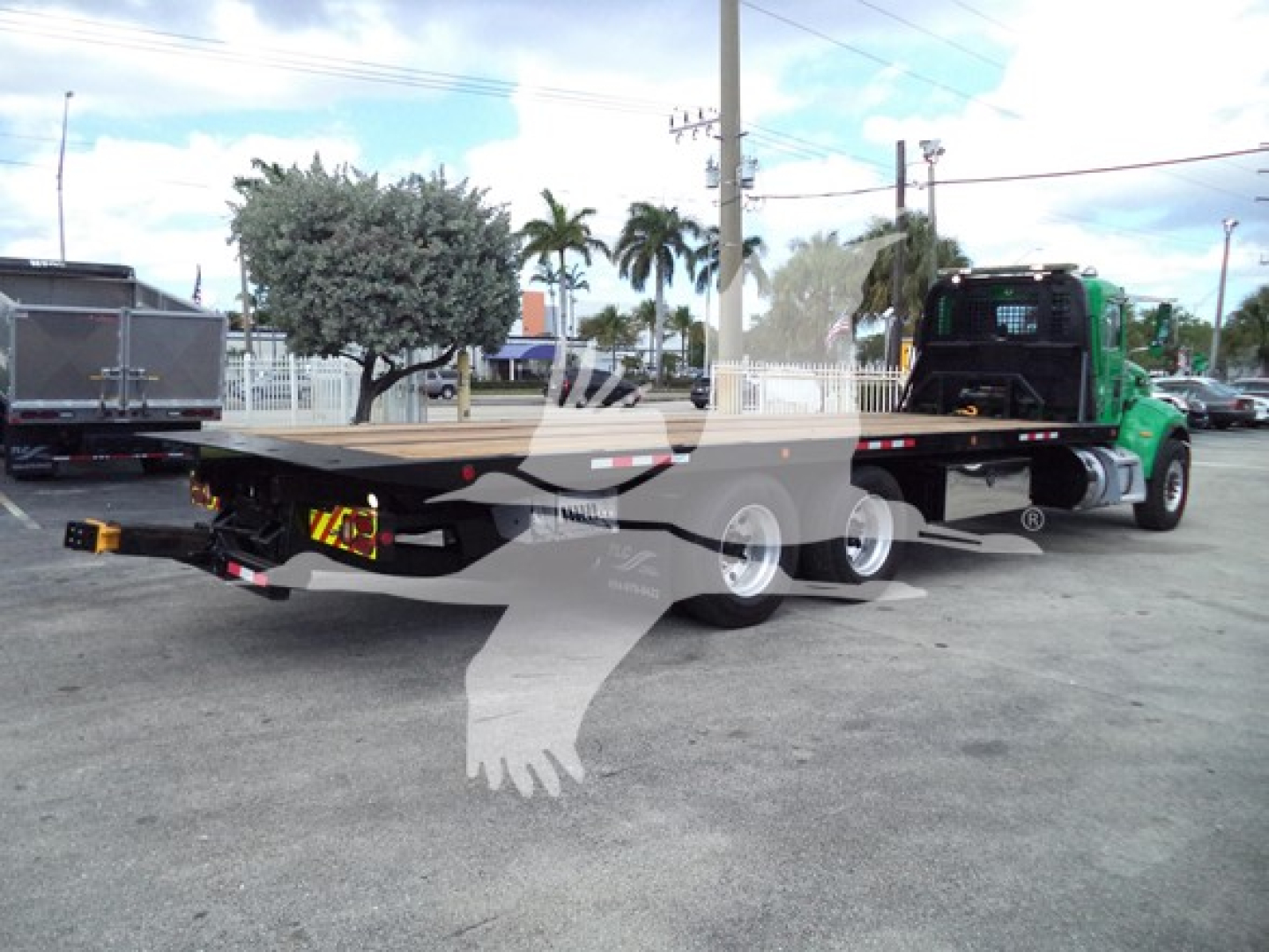 Peterbilt 348 rollback trailer with green tow truck in lot, side view showing flatbed and dual rear axles.