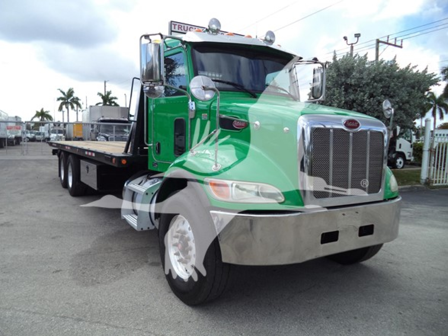 Peterbilt 348 rollback truck in green and chrome front view showing large chrome grille and bumper, dual rear wheels, and flatbed equipment.