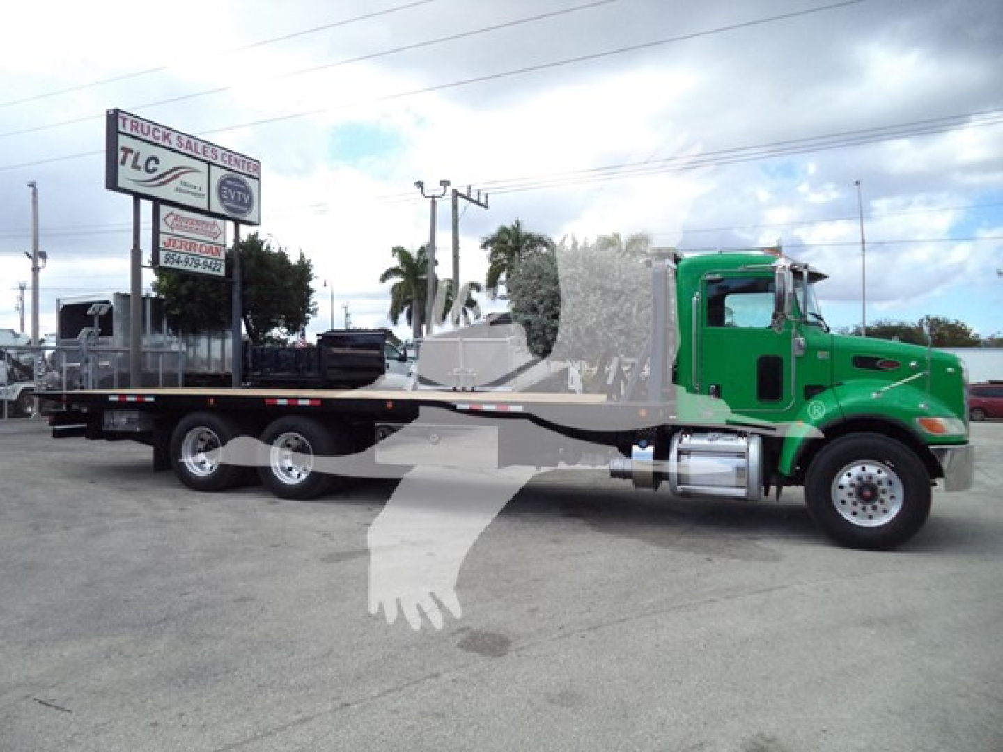 Green Peterbilt 348 rollback truck with a long flatbed and a chrome exhaust, text on a sign in background.