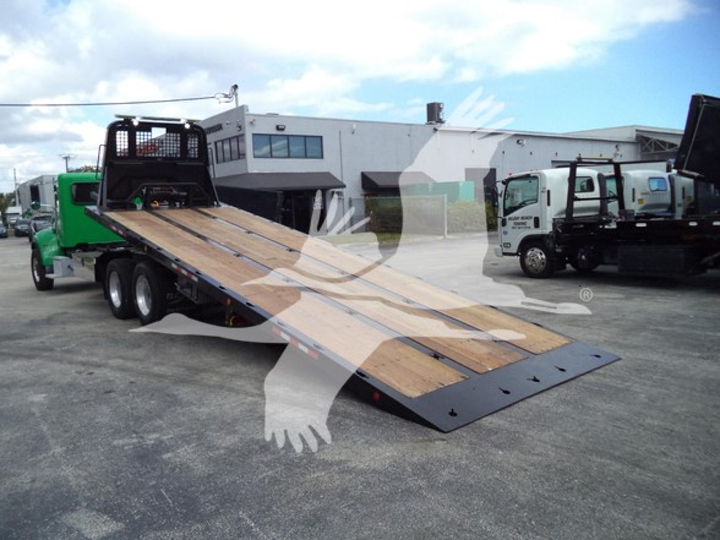 Peterbilt 348 rollback truck with lowered loading bed in a dealership lot showing a steel and wood ramp.