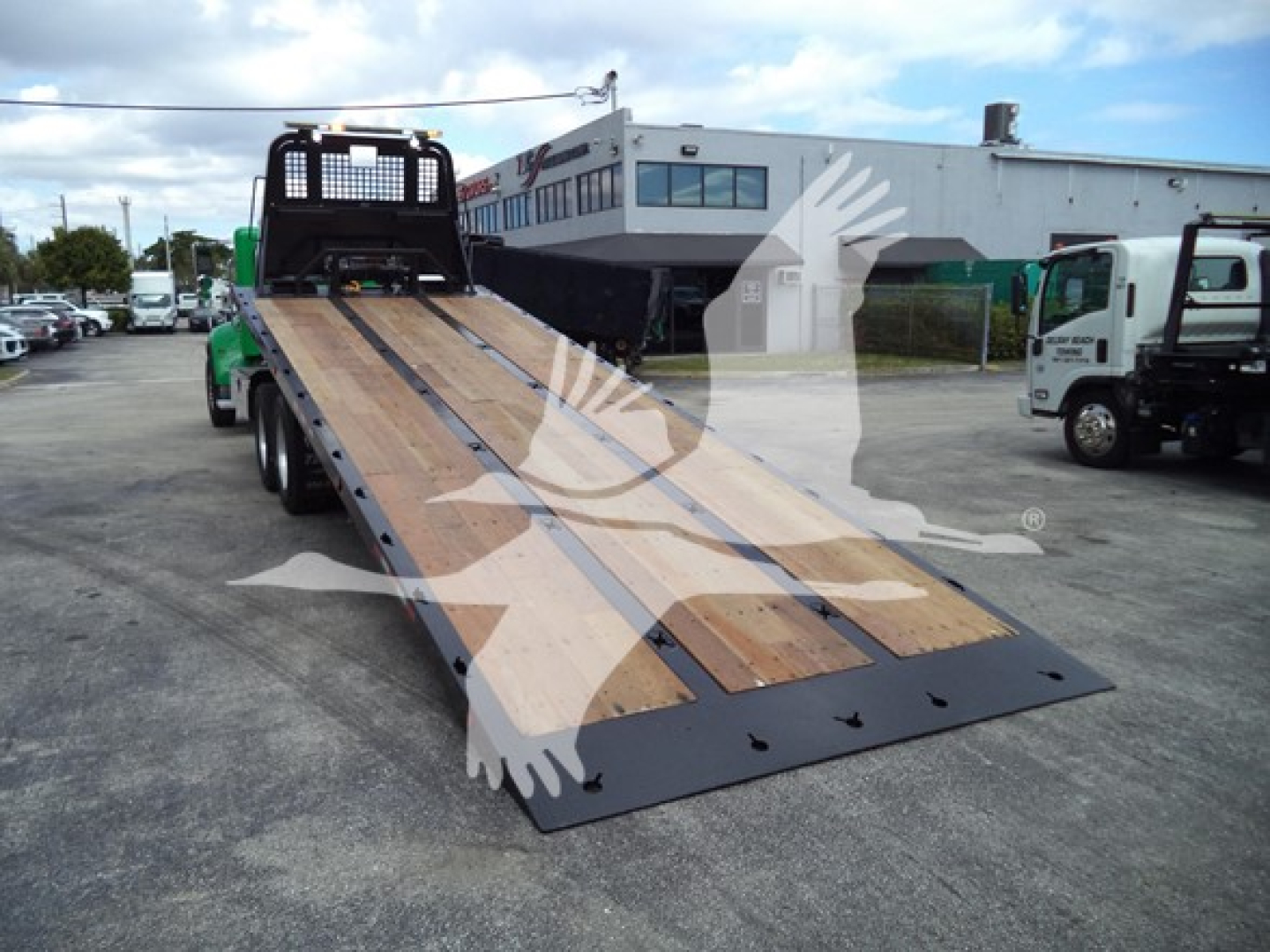 Peterbilt rollback truck with a long ramps bed and metal sides, viewed from the rear/side in a dealership lot.