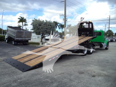 2016 Peterbilt 348 Rollback truck with wooden inclined tilt bed, green cab, and black steel ramp; background shows a dump truck and palm trees.