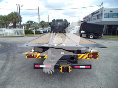 Flatbed rollback truck rear view showing chrome frame and towing hitch with yellow hook and reflective red/white markings.