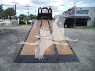 Peterbilt 348 rollback truck bed with wooden platform and ramps, viewed from rear, dealership lot in background.