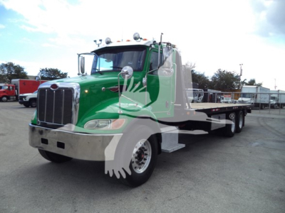 Peterbilt 348 rollback truck in green and black with chrome front, long wheelbase, side steps, and dual rear axles in a dealership lot.