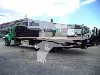 Peterbilt 348 rollback tow truck in yard with flatbed trailer and green cab, side view showing cab and equipment.