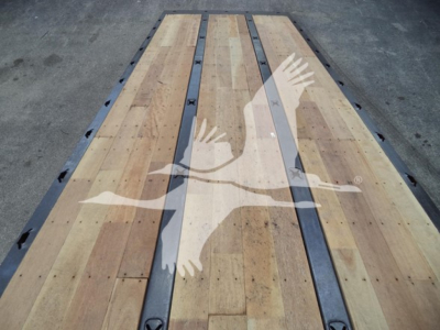 Flatbed truck bed with wooden planks and metal side rails, light reflection of a hand logo across the bed.