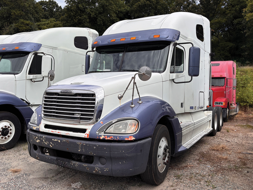 Freightliner CL120 Columbia sleeper cab truck in a used lot showing front grille and headlights with side mirrors and weathered bumper.