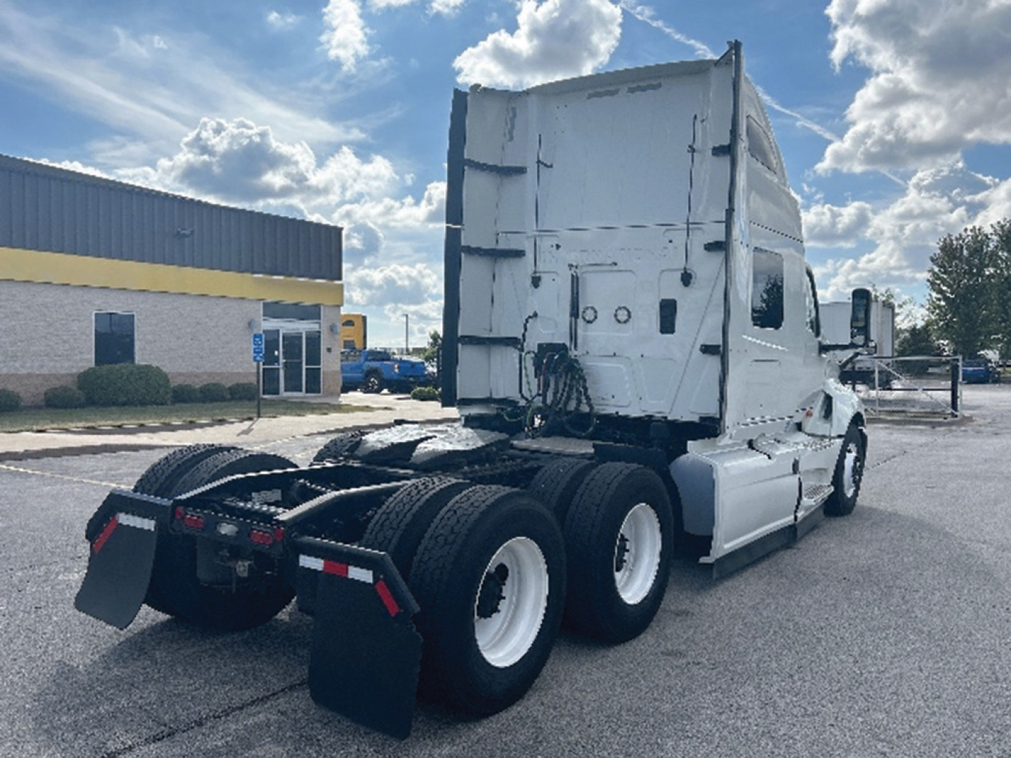 Truck tractor rear view showing fifth wheel, dual rear axles, and cab with tall sleeper, white with black tires.