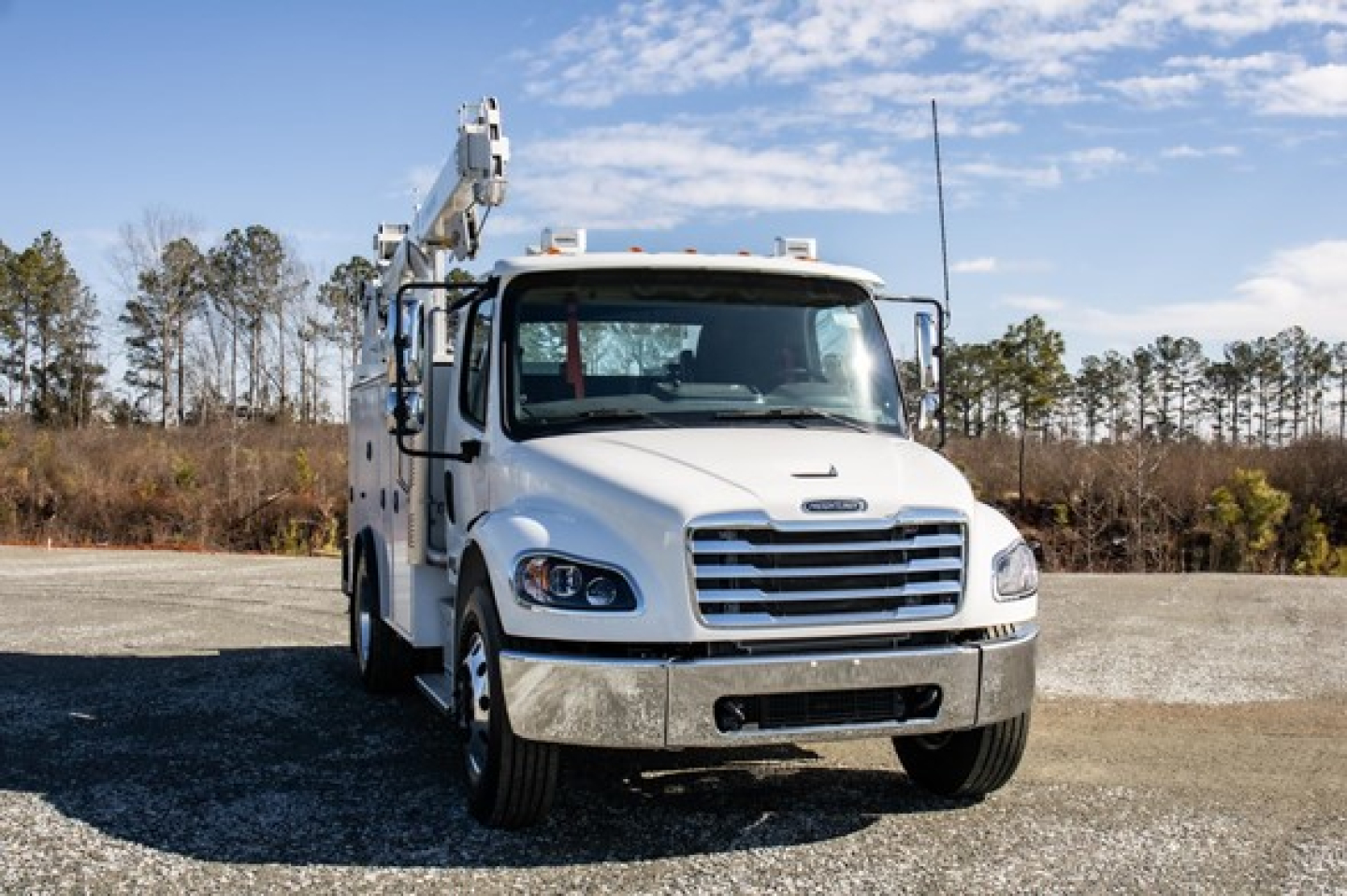 Freightliner M2 106 Plus service truck front view with crane arm folded, white cab, chrome grille, daytime outdoor lot