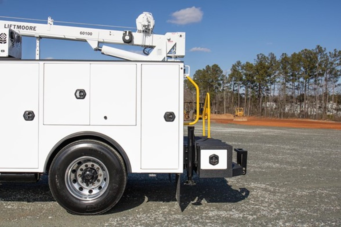 Freightliner service utility truck side view showing storage compartments and LiftMoore aerial lift equipment with white body and black wheel. Visible text includes LIFTMORE on equipment and a small black emblem on a compartment door.