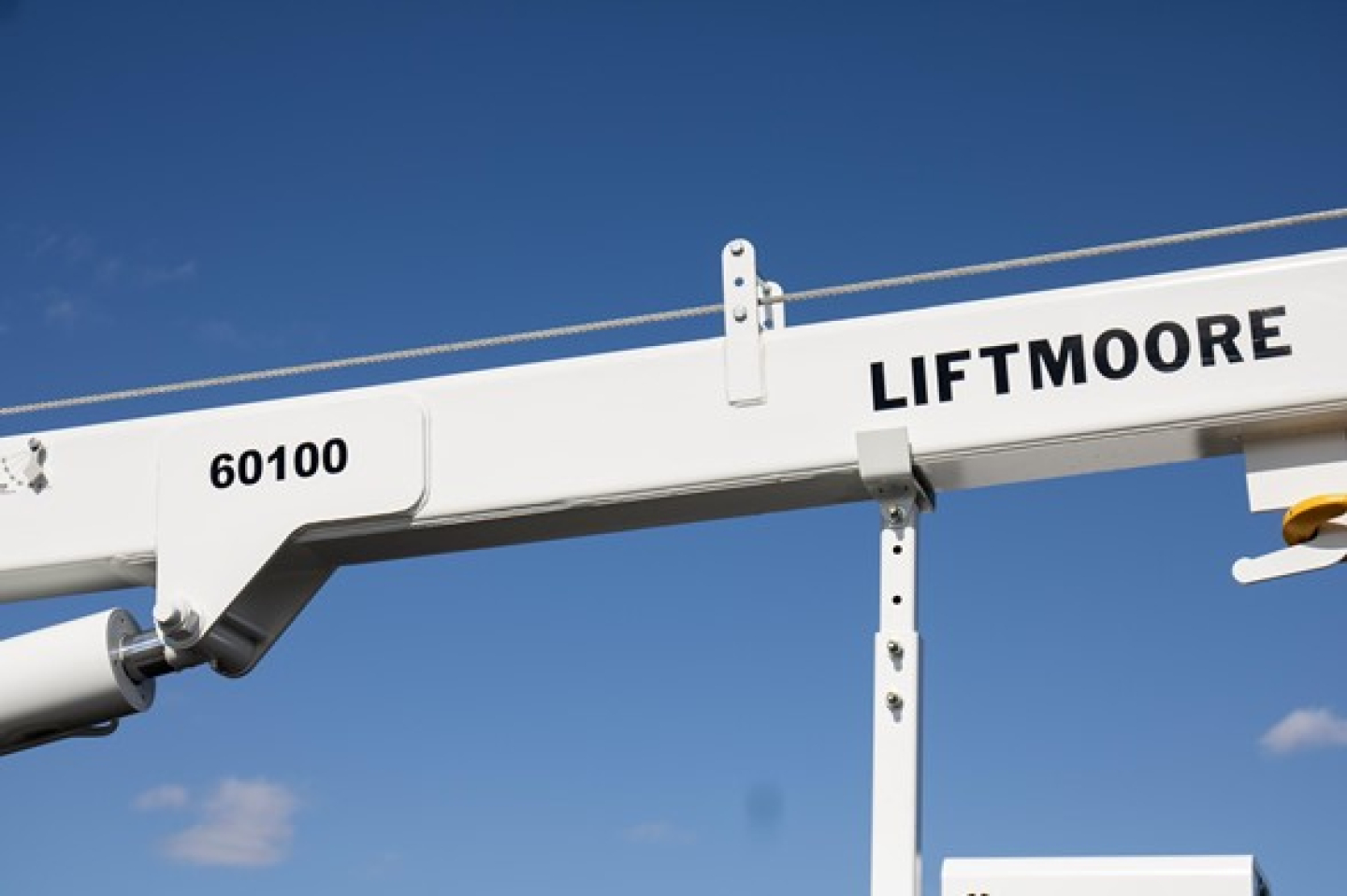 Truck equipment image showing a white structural boom labeled 60100 LIFTMOORE against a blue sky.