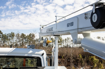 Truck crane arm with Liftrmoore branding and 60100 number on white component; blue sky with trees in background.