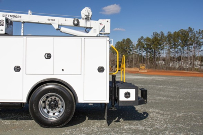 Freightliner service utility truck side view showing storage compartments and LiftMoore aerial lift equipment with white body and black wheel. Visible text includes LIFTMORE on equipment and a small black emblem on a compartment door.