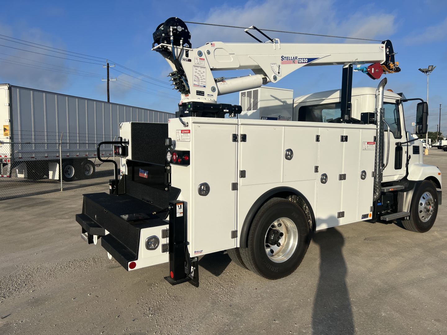 Service/utility truck with crane, white utility body, multiple compartment doors, rear stowage, and mounted crane on top of the truck bed.