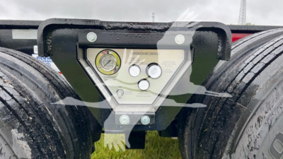 Trailer landing gear area showing toolbox panel with gauges and labels between two wheels of a Fontaine lowboy trailer.